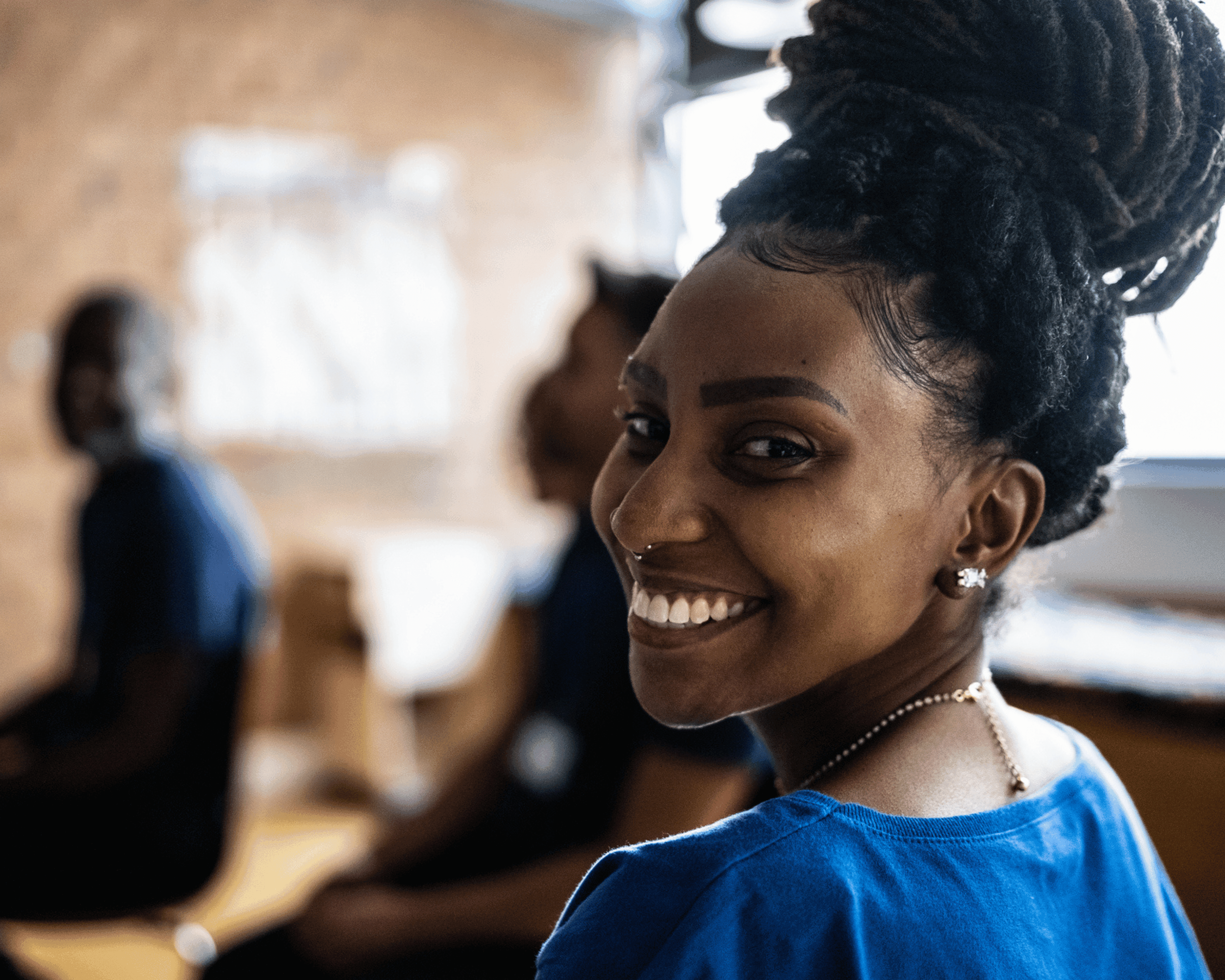 A black woman sitting in a classroom looks back to the camera smiling